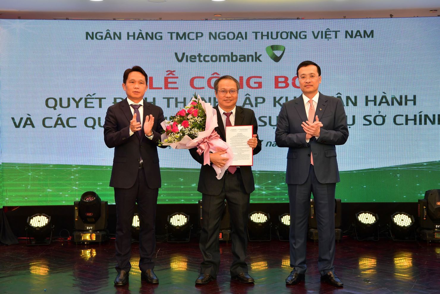 Ông Phạm Quang Dũng - Chủ tịch HĐQT (bên phải) trao quyết định và ông Nguyễn Mạnh Hùng - Thành viên HĐQT tặng hoa chúc mừng tân Trưởng nhóm Nghiên cứu Vietcombank - Tiến sỹ Nguyễn Thắng.